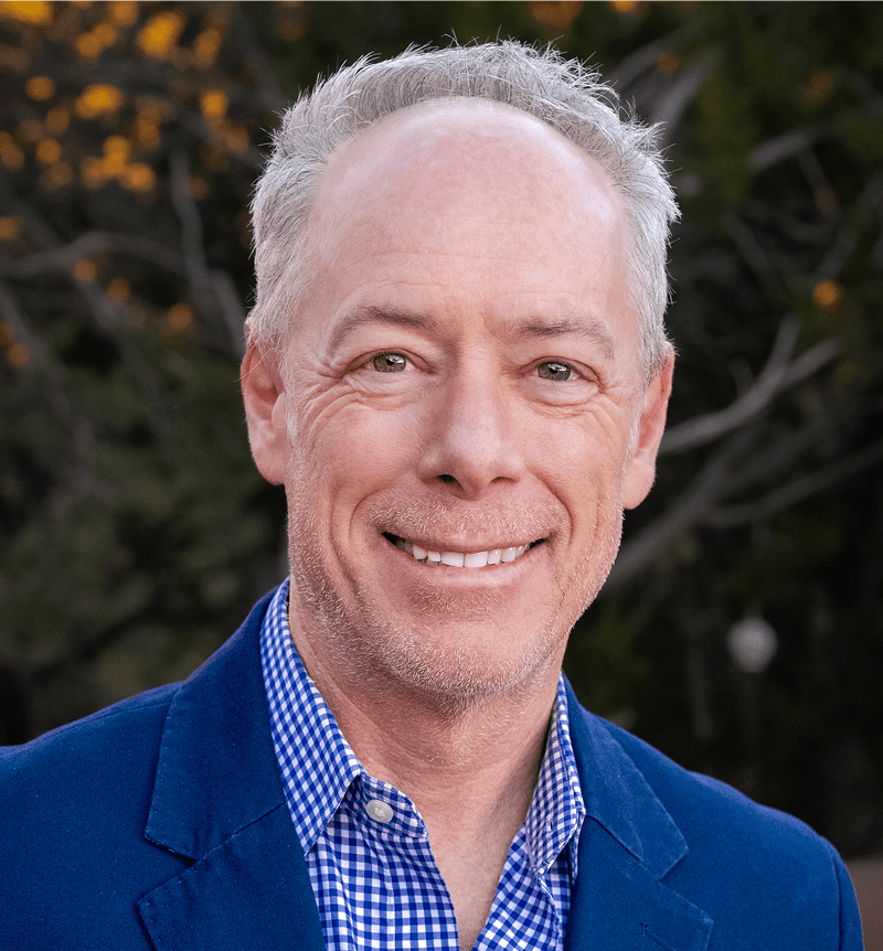 Smiling older man in a blue blazer outdoors.